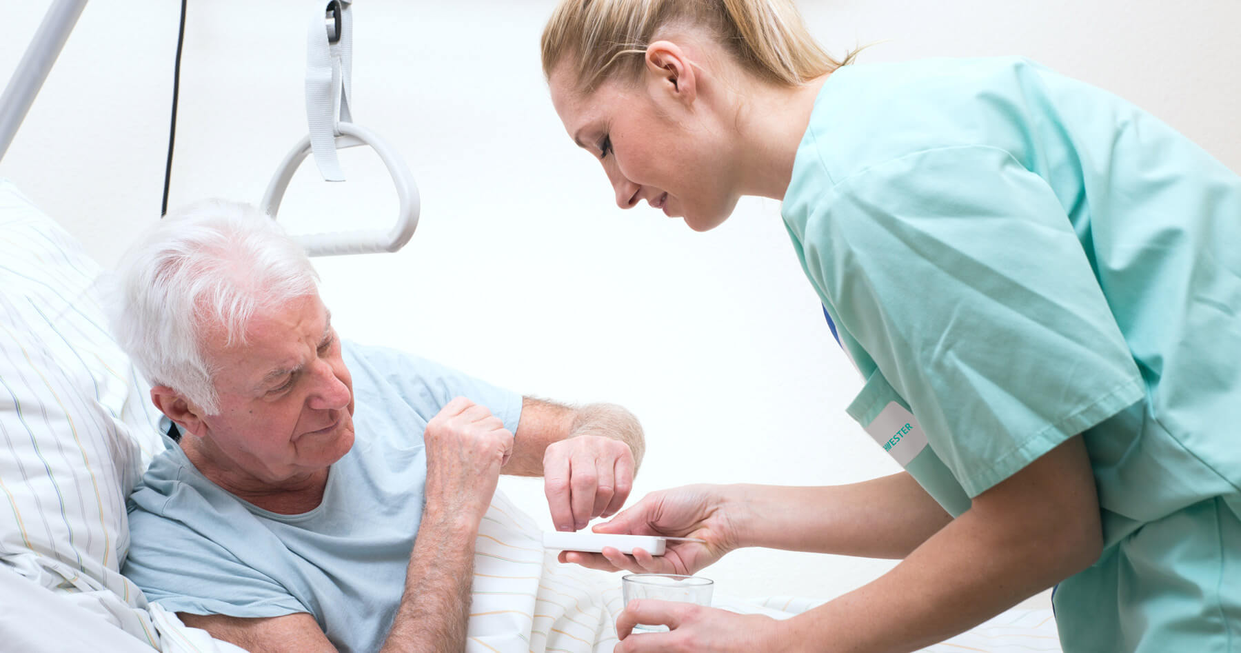 Medikamentenvergabe an einen älteren Herren im Krankenbett
