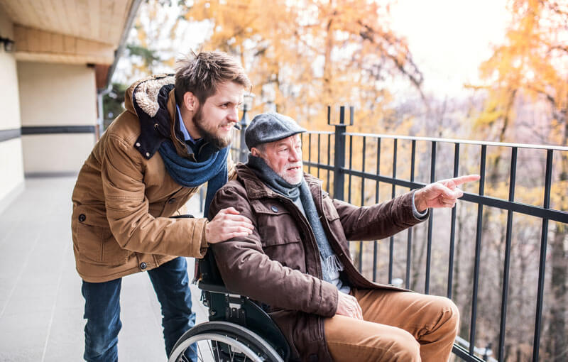 jüngerer Mann unterhält sich mit Senior im Rollstuhl welcher ihm was zeigt