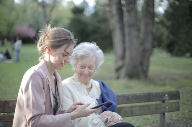 Enkelin zeigt Seniorin etwas am Smartphone